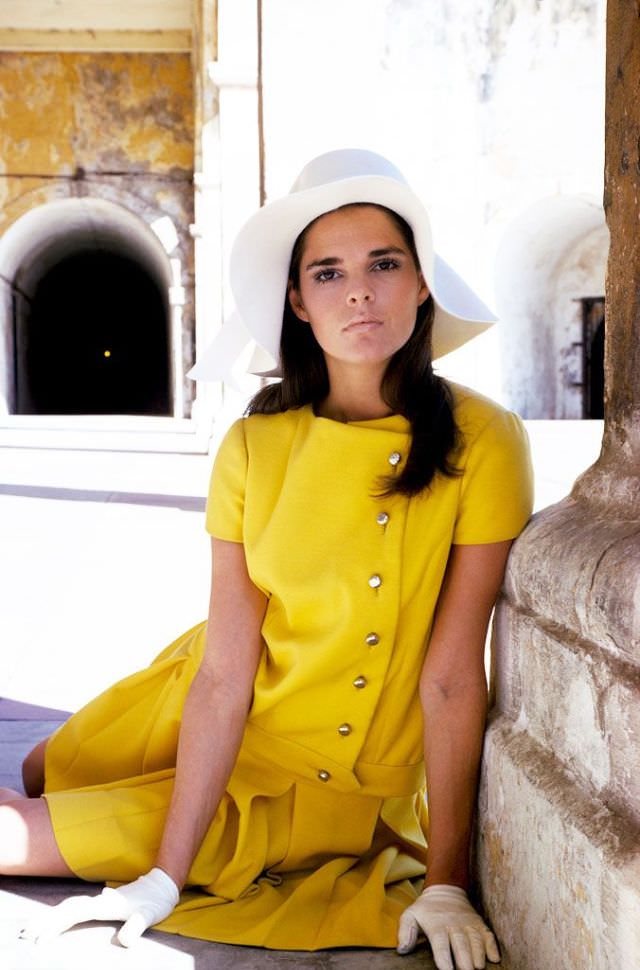 #21 Ali MacGraw is modelling a yellow wool suit by Jacques Tiffeau and with a white felt floppy hat by Emme, March 1967
