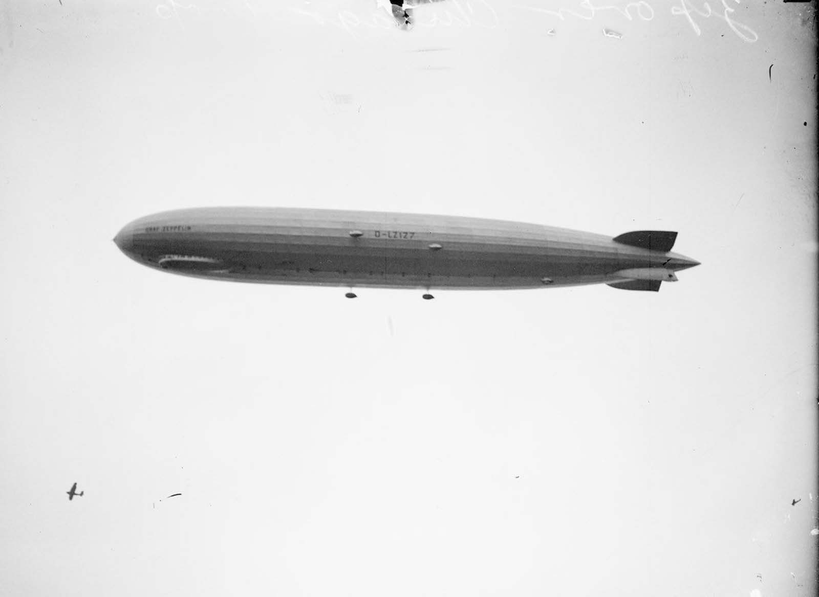 #11 The Graf Zeppelin flies over Chicago, Illinois. An airplane is visible below the Zeppelin on the lower left half of the image.