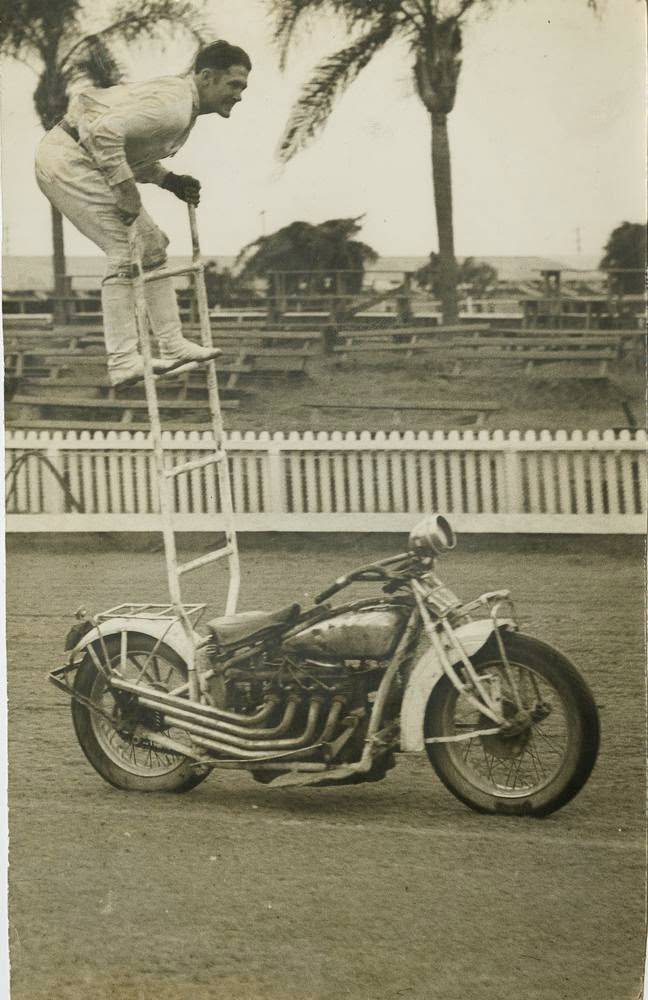 #3 A young man is at the top of a small ladder attached to his motorcycle, 1955.