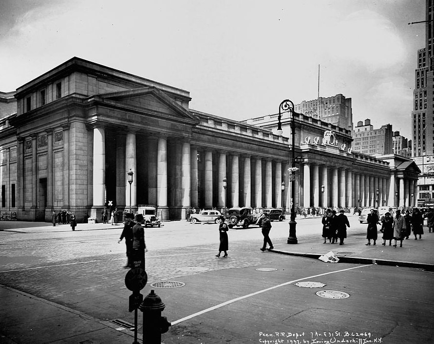 #52 Pedestrians and cars bustle past the doric colonnade of Pennsylvania Station.