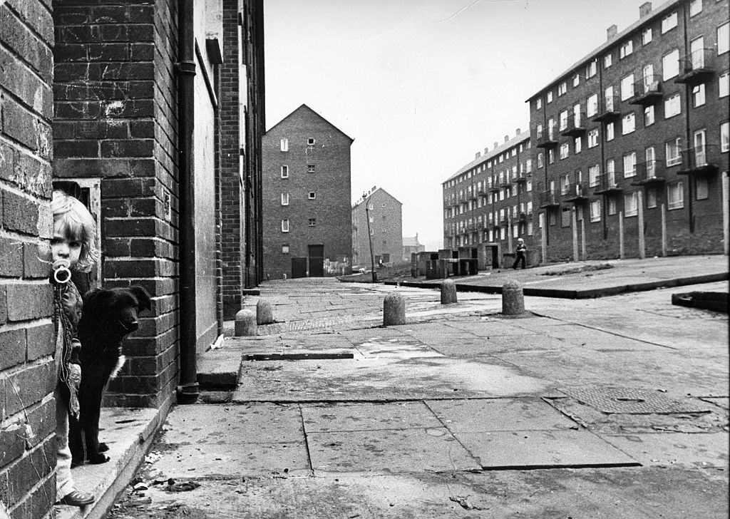 #44 Derelict housing in an area of Newcastle – A little girl and her pet dog play in the street, 1970s