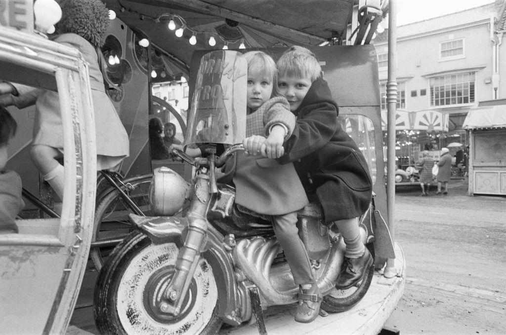 #77 Brother and sister riding a motorcycle on a child’s roundabout at the Northallerton May Fair 1971.
