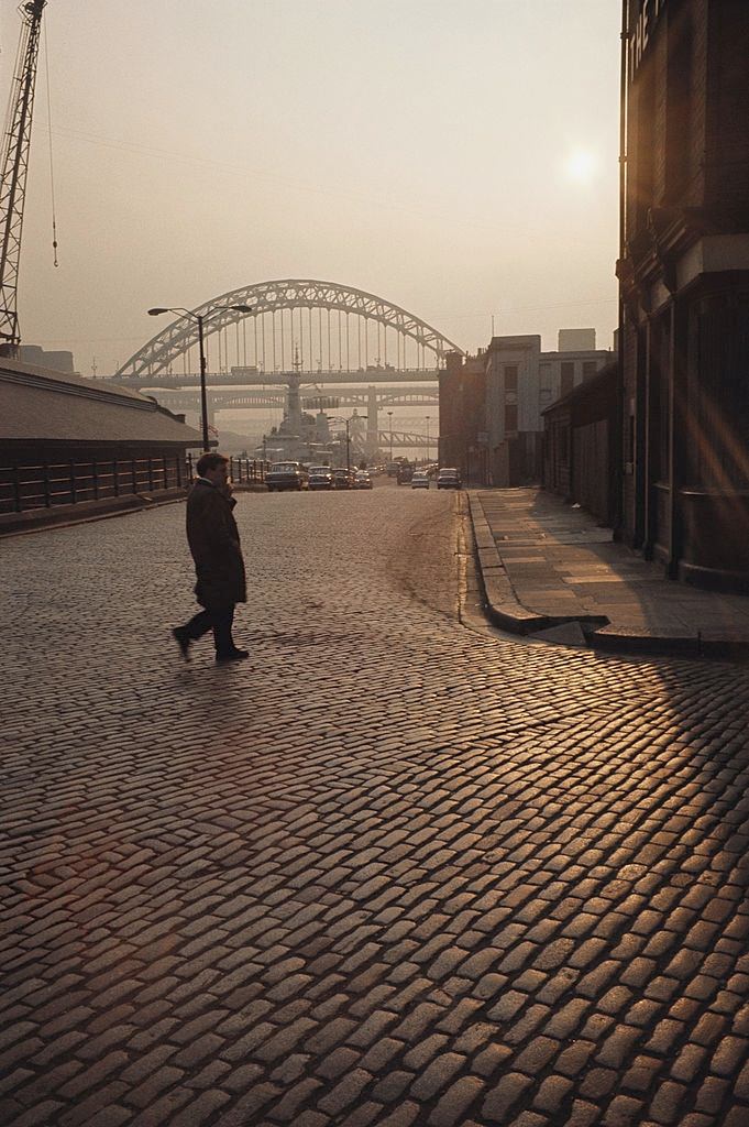 #88 A lone man walks across the cobbled street in view of the Tyne bridge, Newcastle, 1970.