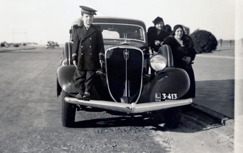 A little boy in a sailor’s uniform standing on the bumper of a 1934 Studebaker Land Cruiser.