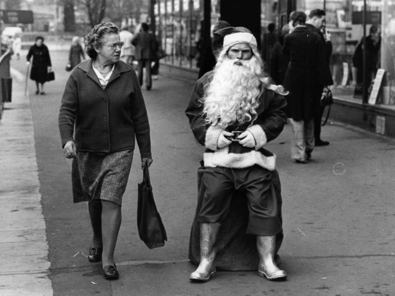 #20 A woman glance at a surly looking Santa in a busy shopping street, 1975.