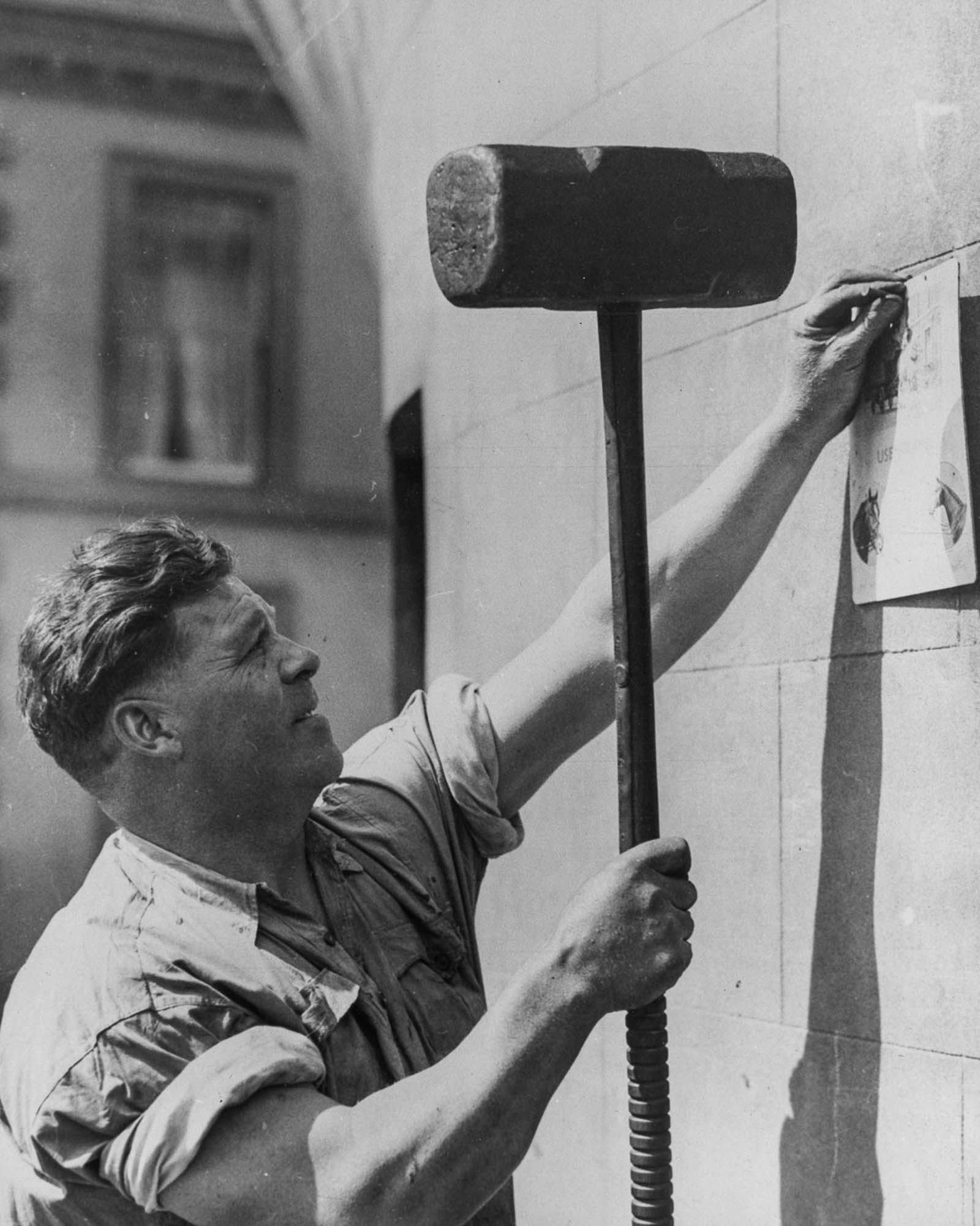 #16 Joe Price uses a 50-pound hammer to nail up a notice, 1934.