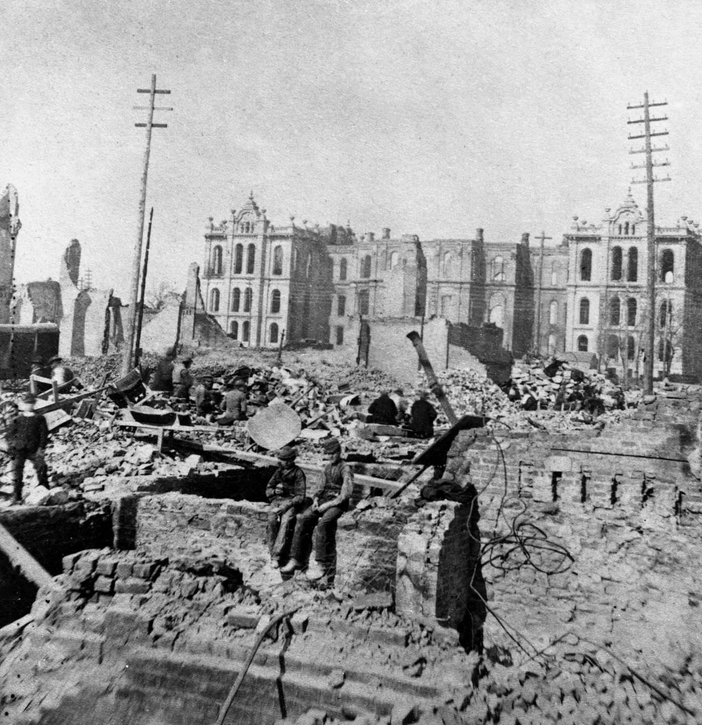 #51 Two boys sit on top of a partial stone wall in the wreckage of a burned-out building at Madison and Clark Streets, with the Court House in the background following the fire.