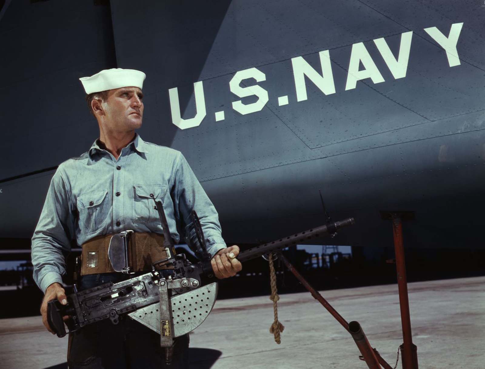 #18 J.D. Estes, a seven-year veteran of the Navy, hefts a machine gun to be installed in a plane.