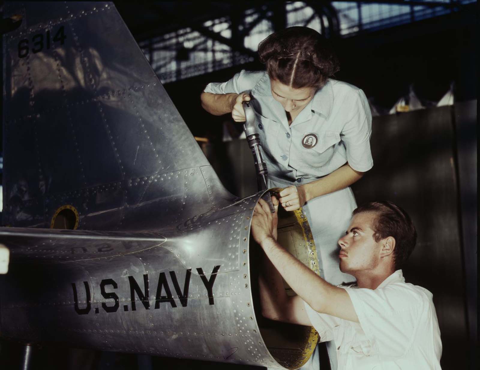#4 Virginia Davis, a riveter in the assembly and repair department of the Naval Air Base, supervises Charles Potter, an NYA trainee from Michigan.
