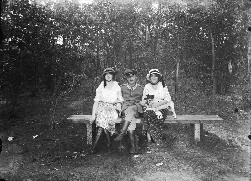#23 Bench in the woods, with a German soldier flanked by two women. The woman on the right has a dog on her lap, 1916