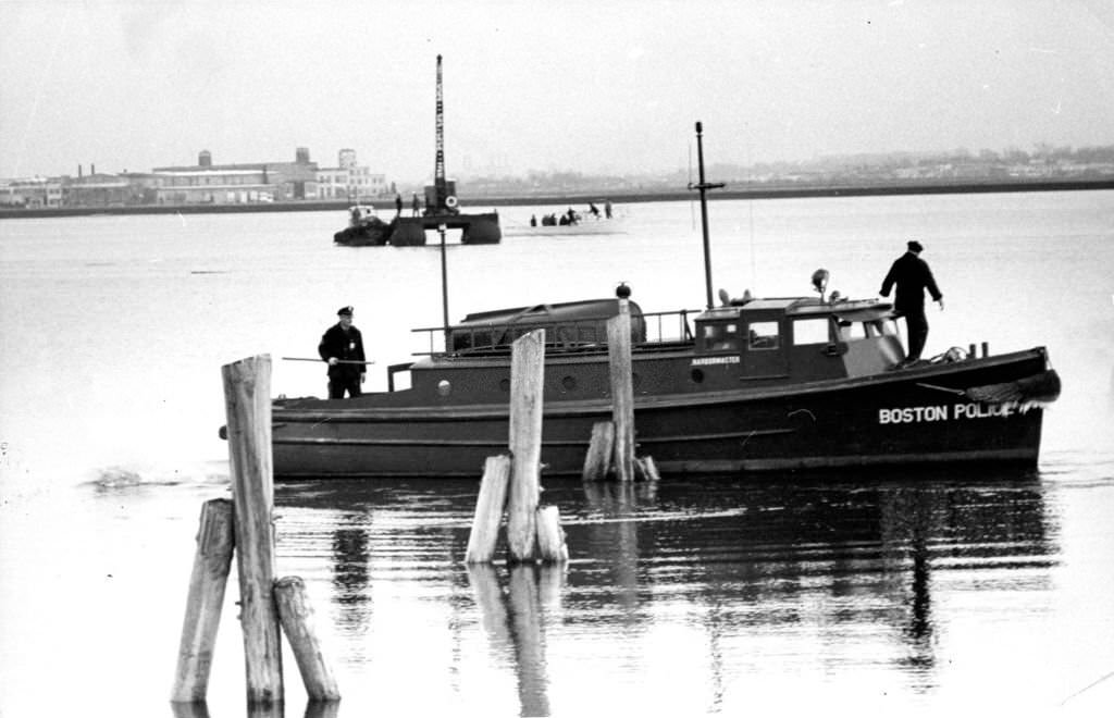 #154 Boston Police officers search for a boat which sank after a fire near the Savin Hill Yacht Club in Boston’s Dorchester, 1962.