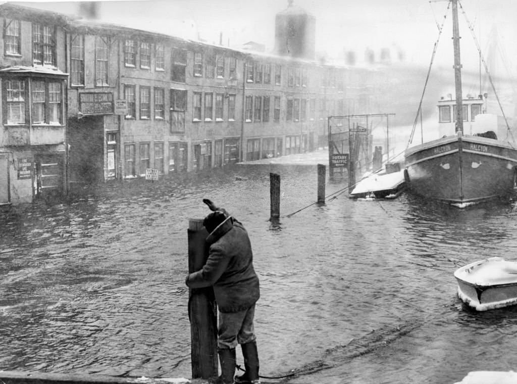 #53 A fisherman secures a boat at T Wharf in Boston as tidal waters flood nearby houses on Jan. 20, 1961.