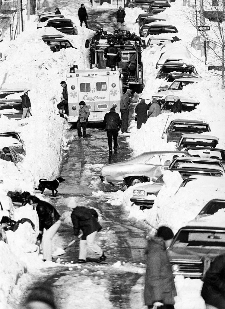 #117 An ambulance, a fire truck, and snow shovelers all occupy Putnam Street in East Boston, 1978.