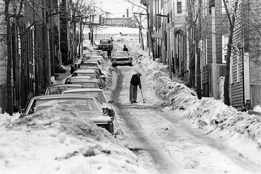 #125 A man hacks at ice on a rutted Soley Street in Boston’s Charlestown, 1977.