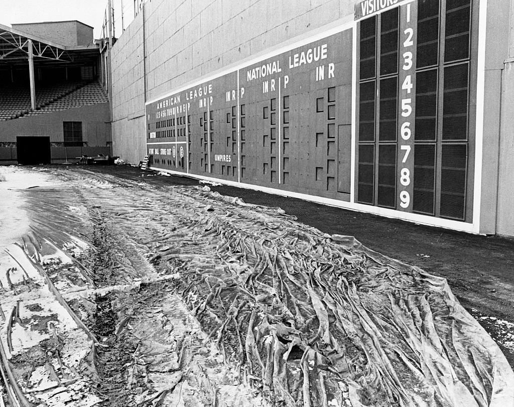 #163 Snow removal has begun at Fenway Park, with the field now showing through the sea of plastic covering it, seen near the scoreboard on March 12, 1969.