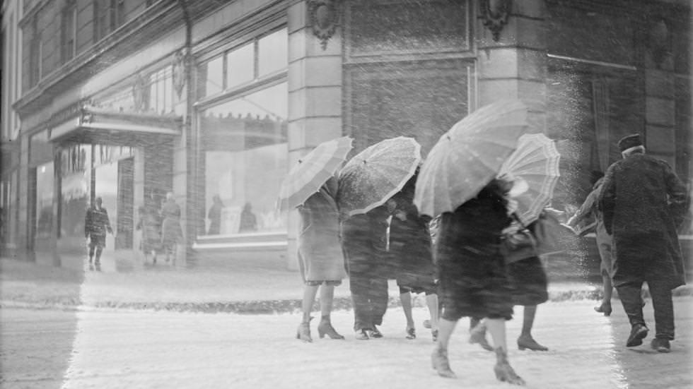 #18 Women use umbrellas to ward off snow, during snowstorm in downtown Boston, 1930