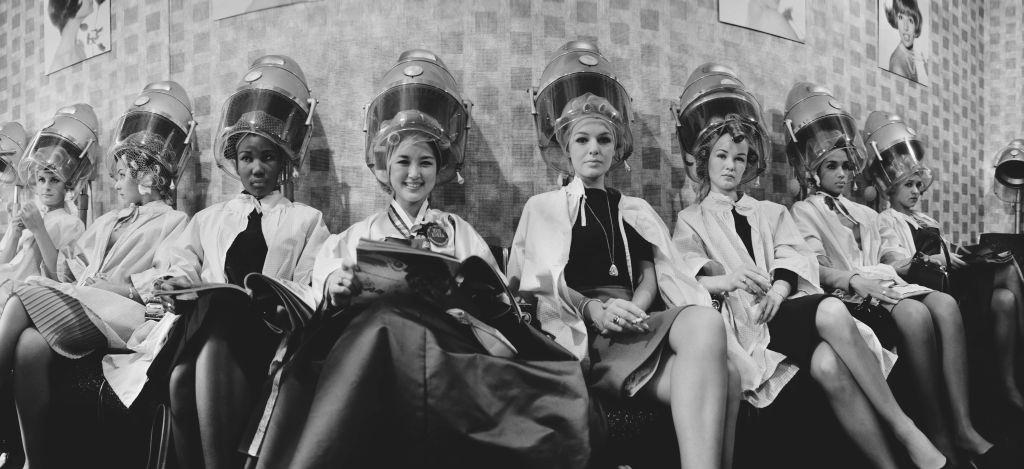 #2 Contestants for the upcoming Miss World beauty pageant seated under hairdryers at a hairdressing salon in London on 12th November 1964.