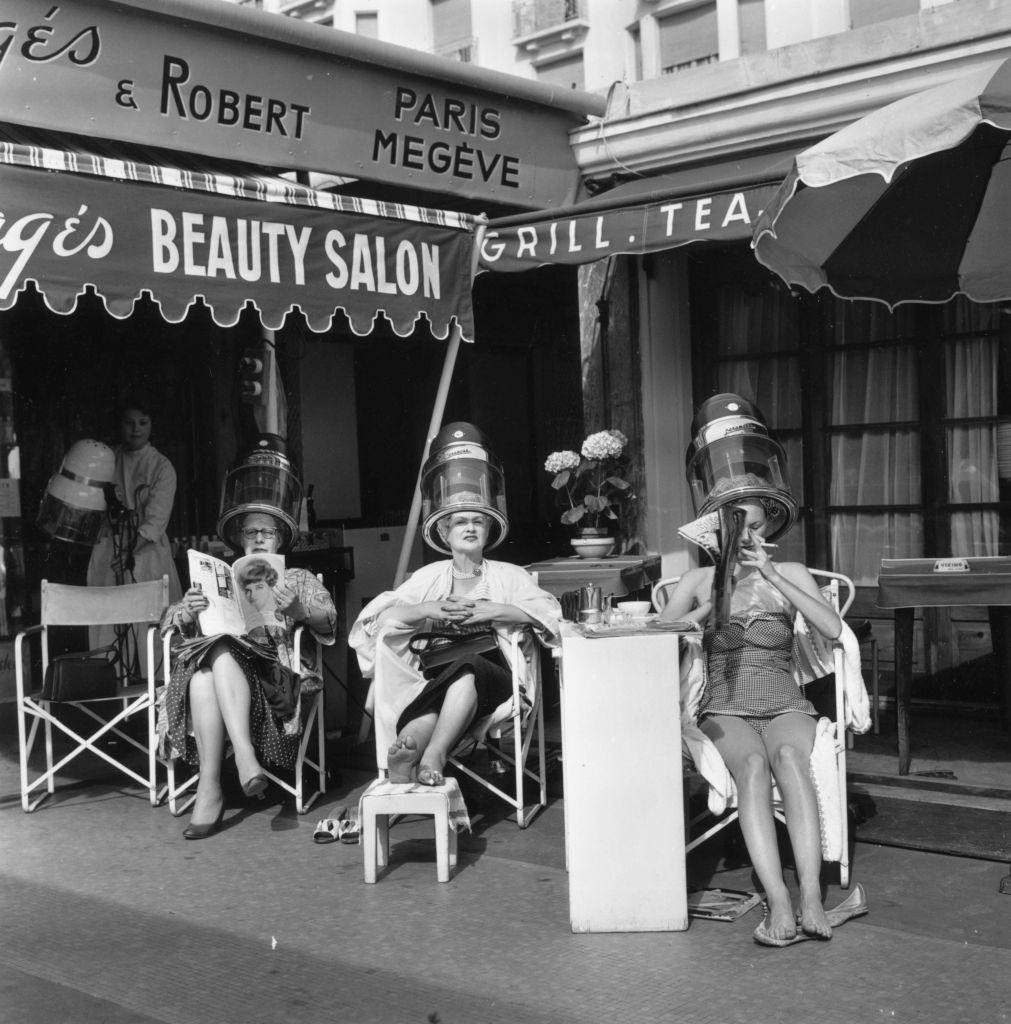 #40 Visitors sit beneath the dryers at an open air hairdressing salon overlooking the Mediterranean Sea during the Cannes Film Festival, 1958