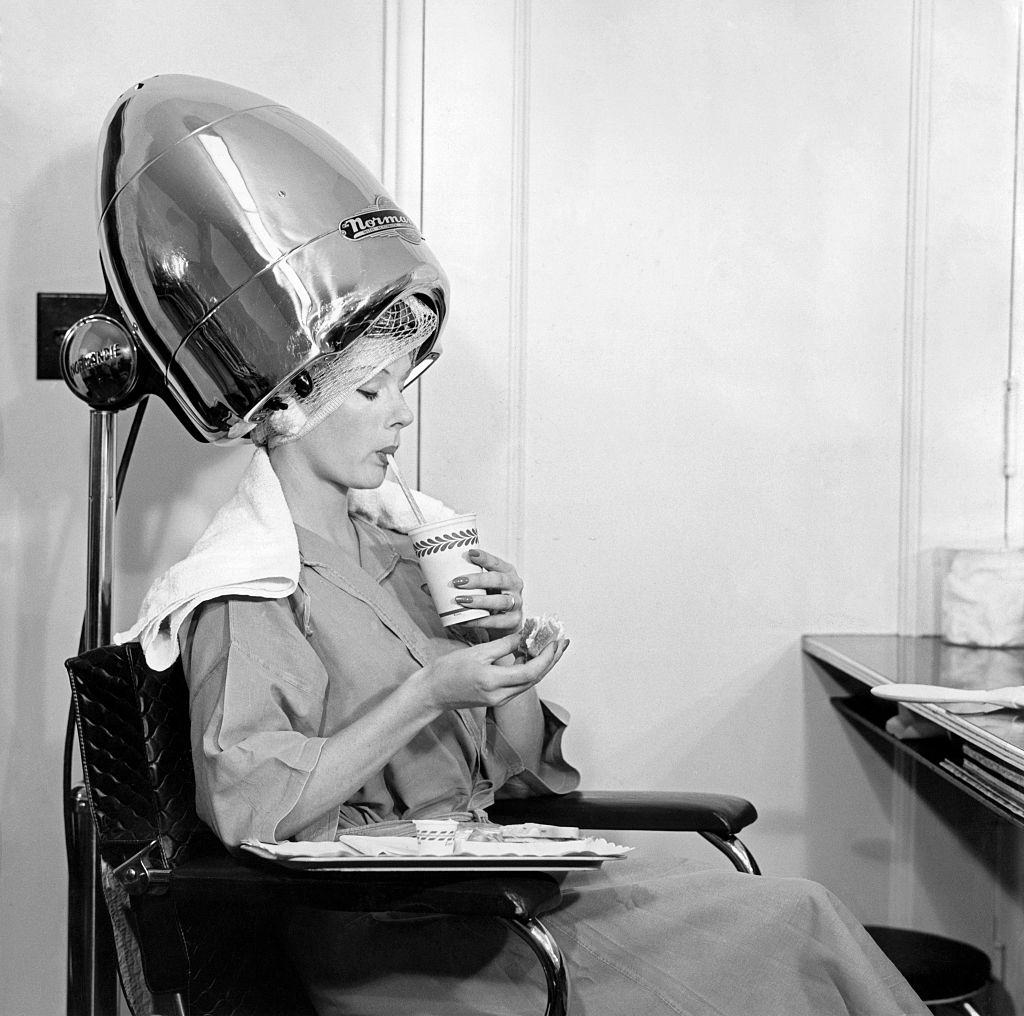 #48 A woman drinking something under a hair drier, 1960s