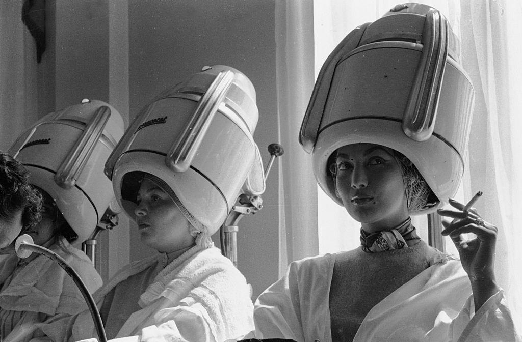 #50 Spanish fashion model, Teresita Montes, sister of the film star Maria Montes, sitting under a Parisian beauty salon’s hairdryer smoking a cigarette, 1955