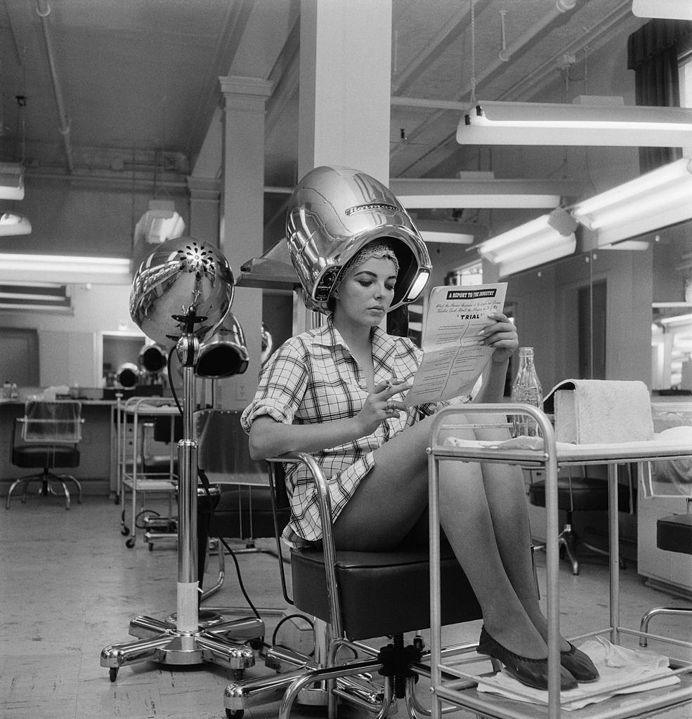 #51 English actress Joan Collins waits for her hair to dry in a film studio, 15th August 1955.