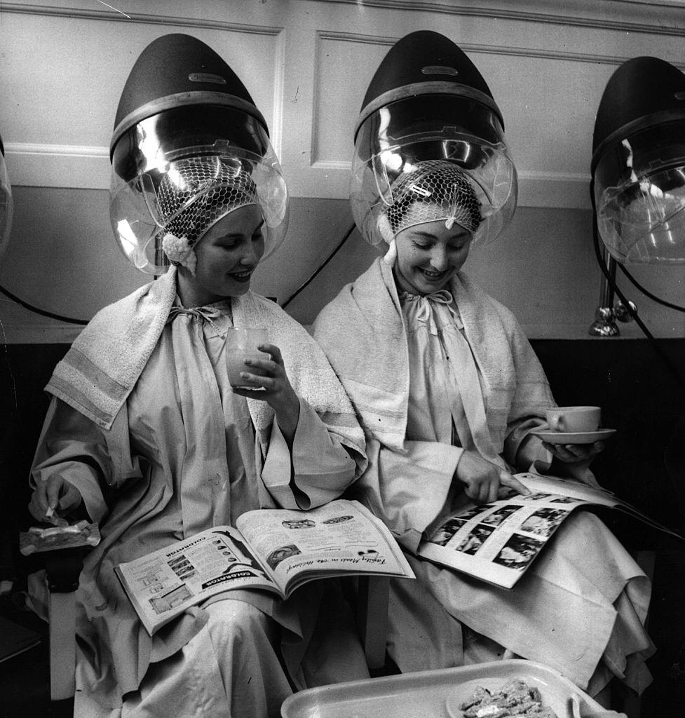 #56 Two women sitting under hairdryers as they wait for their ‘perms’ to set, 1954