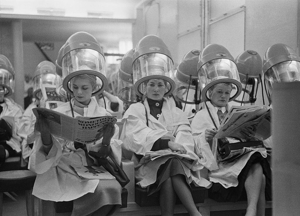 #58 A row of British women sitting under hairdryers in a Paris salon, 1954