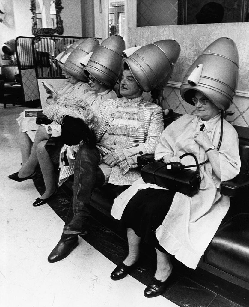 #7 A famous television hairdresser Raymond Bessone, known as ‘Teazy Weazy’, sitting under a hairdryer with a group of ladies at his salon, 1969