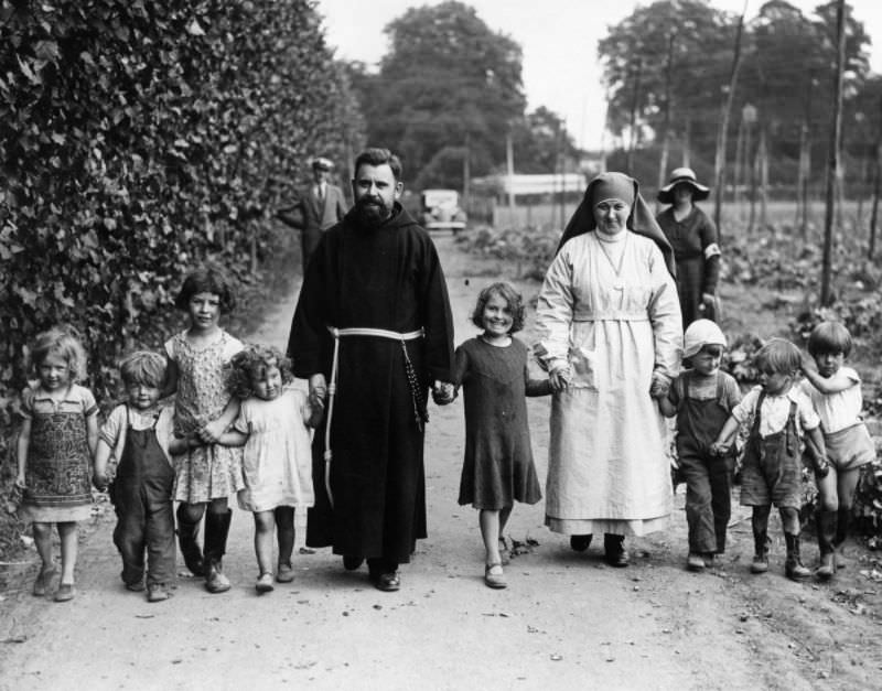 #15 A Franciscan friar and nun walk with hop pickers’ children at Paddock Wood, Kent, 1934.