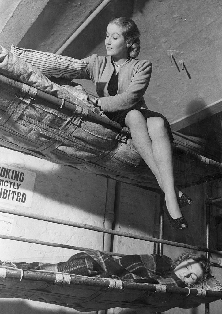 #5 A woman fixes her matress and pillows on the top bunk of her bed as she prepares for a nights sleep in an air raid shelt