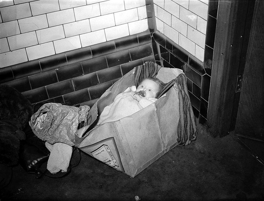 #52 A baby tucked up in a packing case shelters from German daylight bombing deep in a corner of the Piccadilly Underground station.