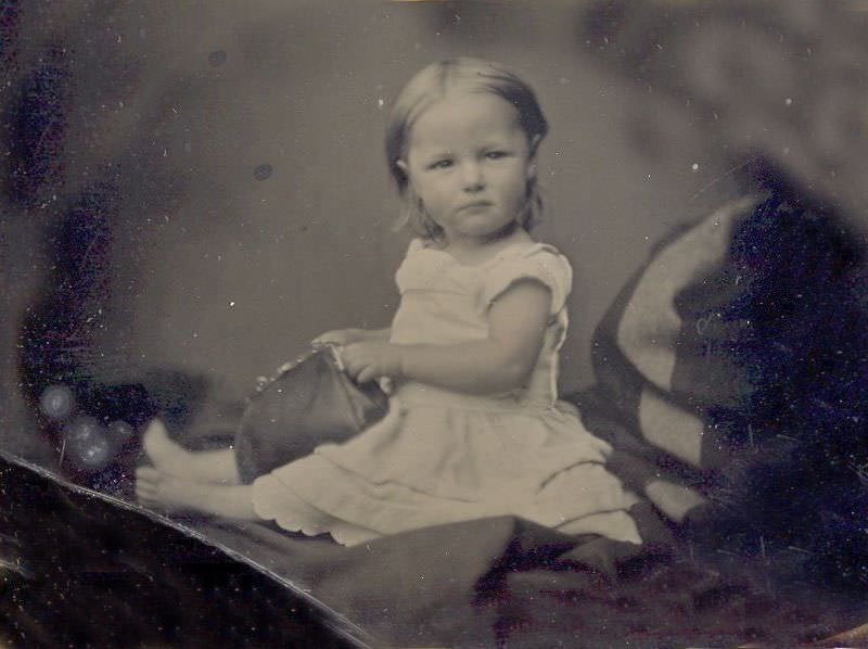 #19 Cute little girl most likely sitting on mom’s lap (hidden under blanket) while playing with her mother’s purse