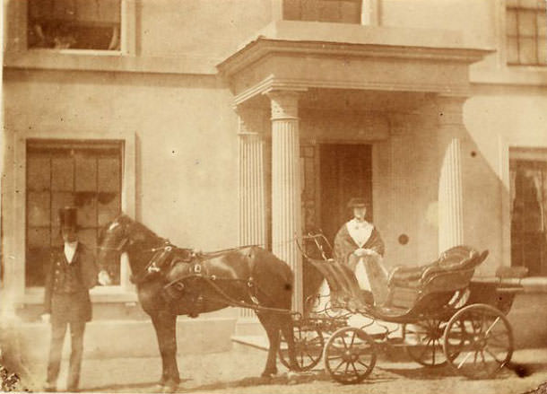 #33 Man, woman and horse-drawn carriage before a colonnaded porch