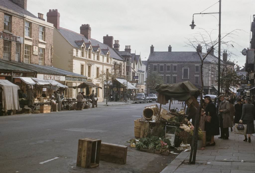 #92 Pedestrians and shoppers buy produce from market stalls lining a main street in the centre of the town of Mold in Flintshire, Wales 1960.