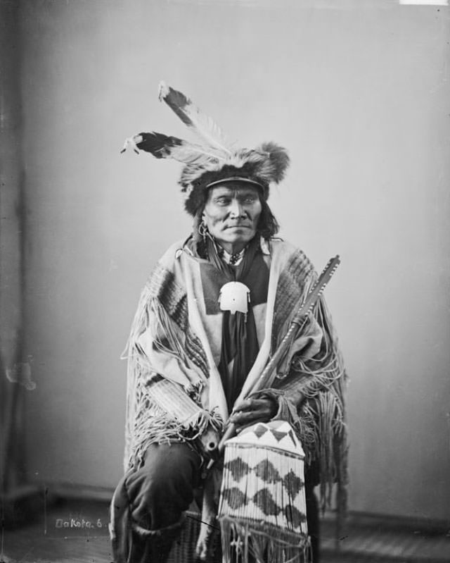 #11 Ta-Tan-Ka-Han-Ska (Long Fox or Long Buffalo Bull) wearing skunk hat and holding pipe and beaded and quilled bag.