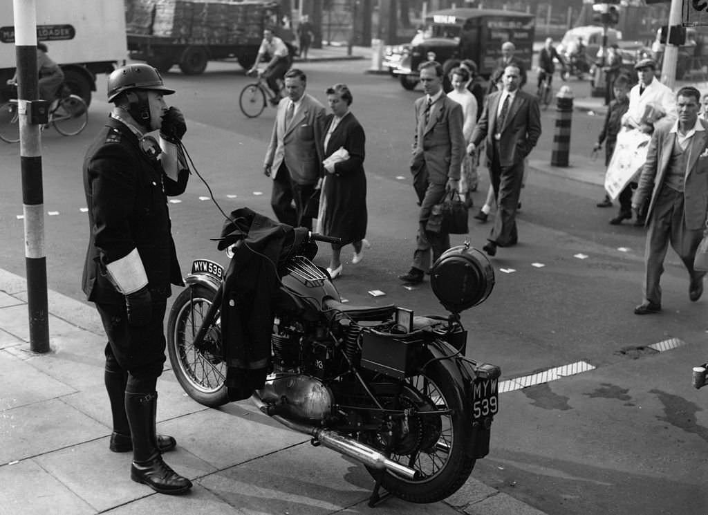 #119 A police motorcyclist gives safety-first instructions to pedestrians at Kennington Oval, 1955