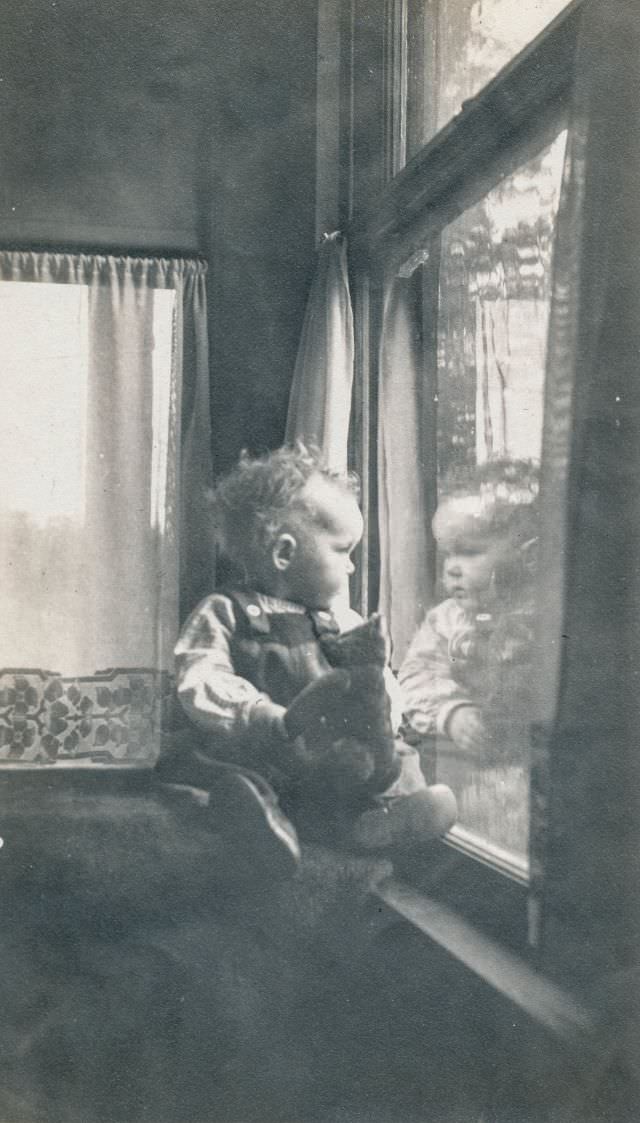 #26 Baby looks out of a window while holding a teddy bear