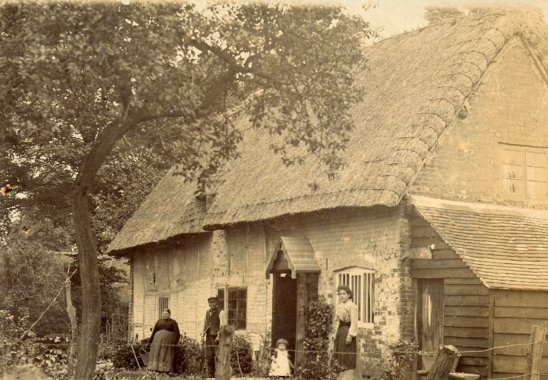 #18 Family stand outside thatched house