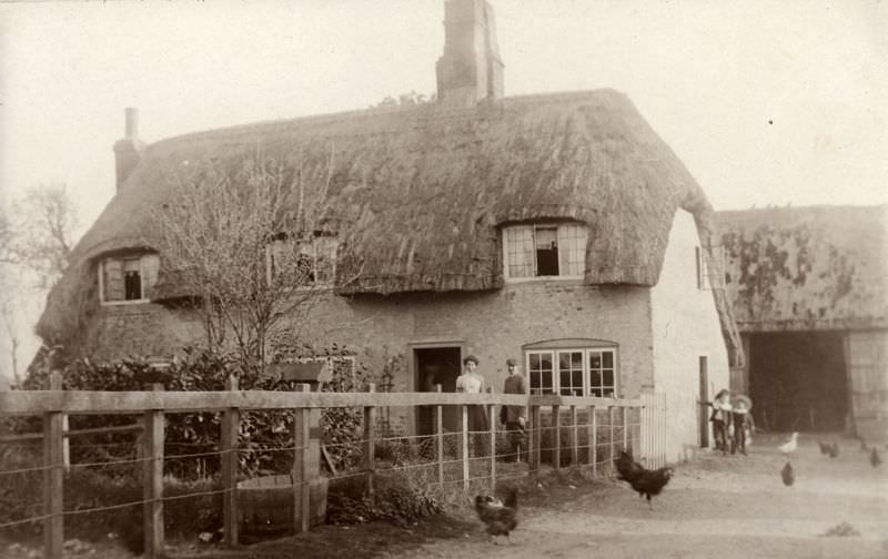 #42 The farmers stand outside the front door and their children at the side with the hens and ducks pecking about