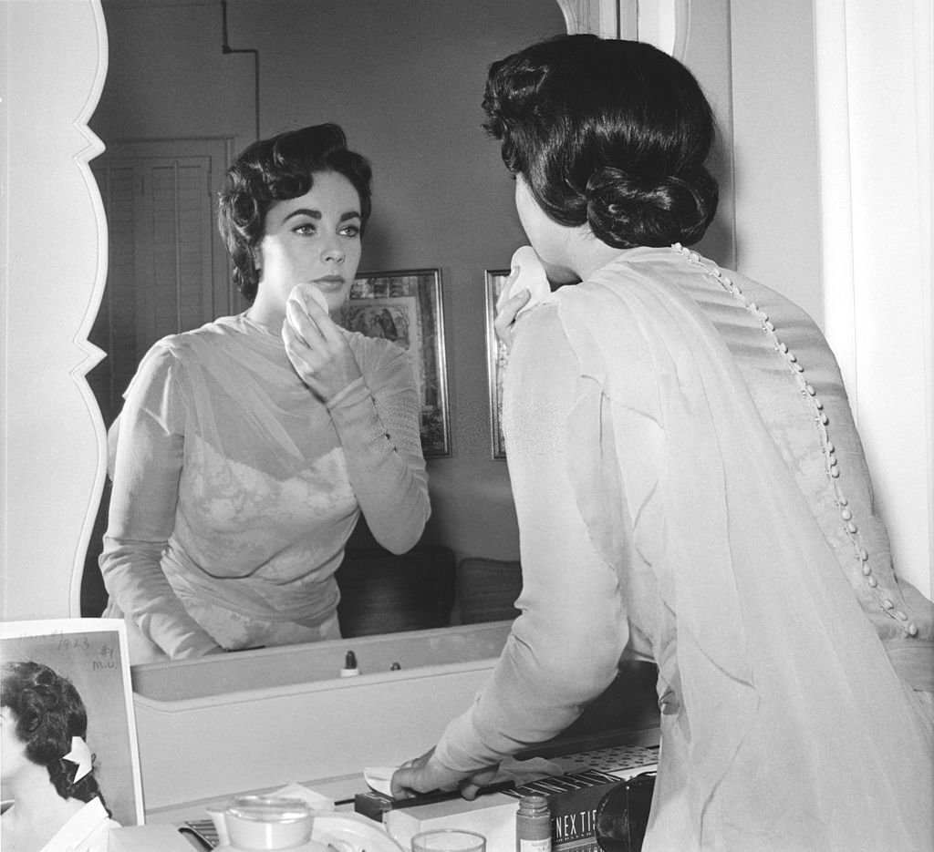 #18 Elizabeth Taylor applies make-up in front of a mirror while on the set ‘Giant’