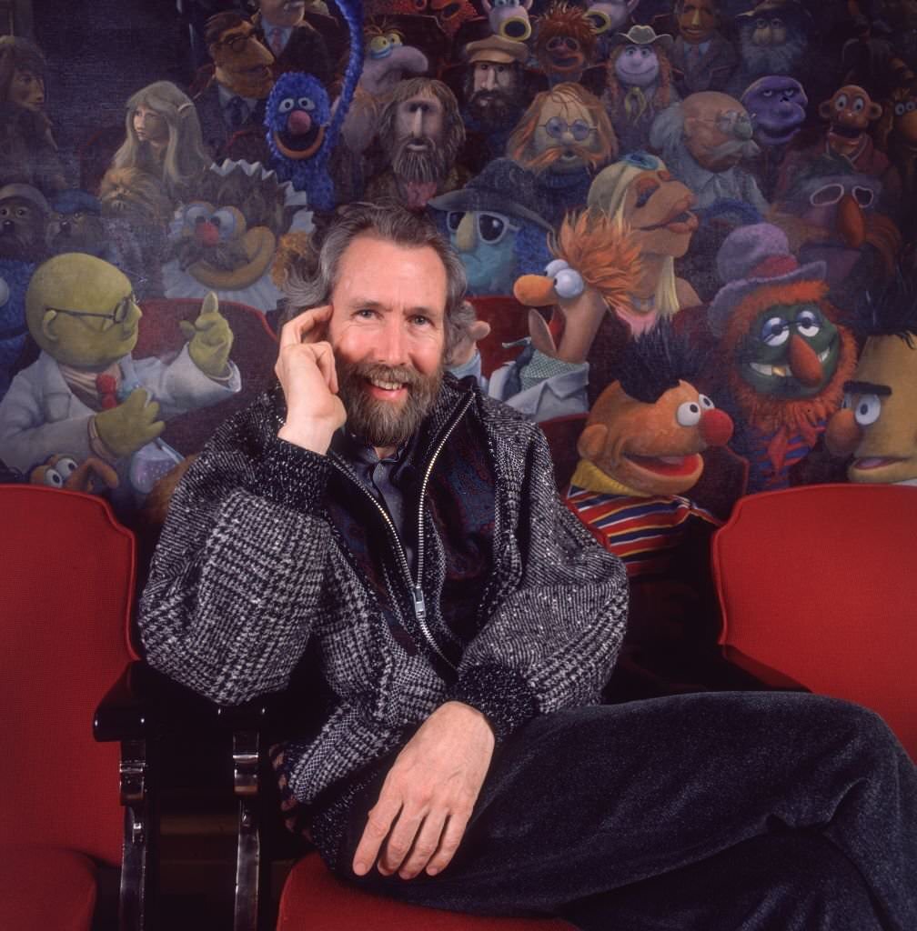 #17 Jim Henson sitting in a theater chair in front of a painting of his creation, The Muppets.