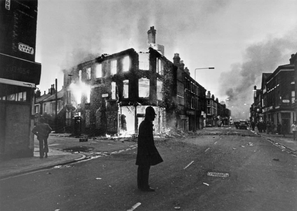 #73 A police officer is silhouetted against a background of a burning building during riots in the Toxteth area of Liverpool, England, 8th July 1981.