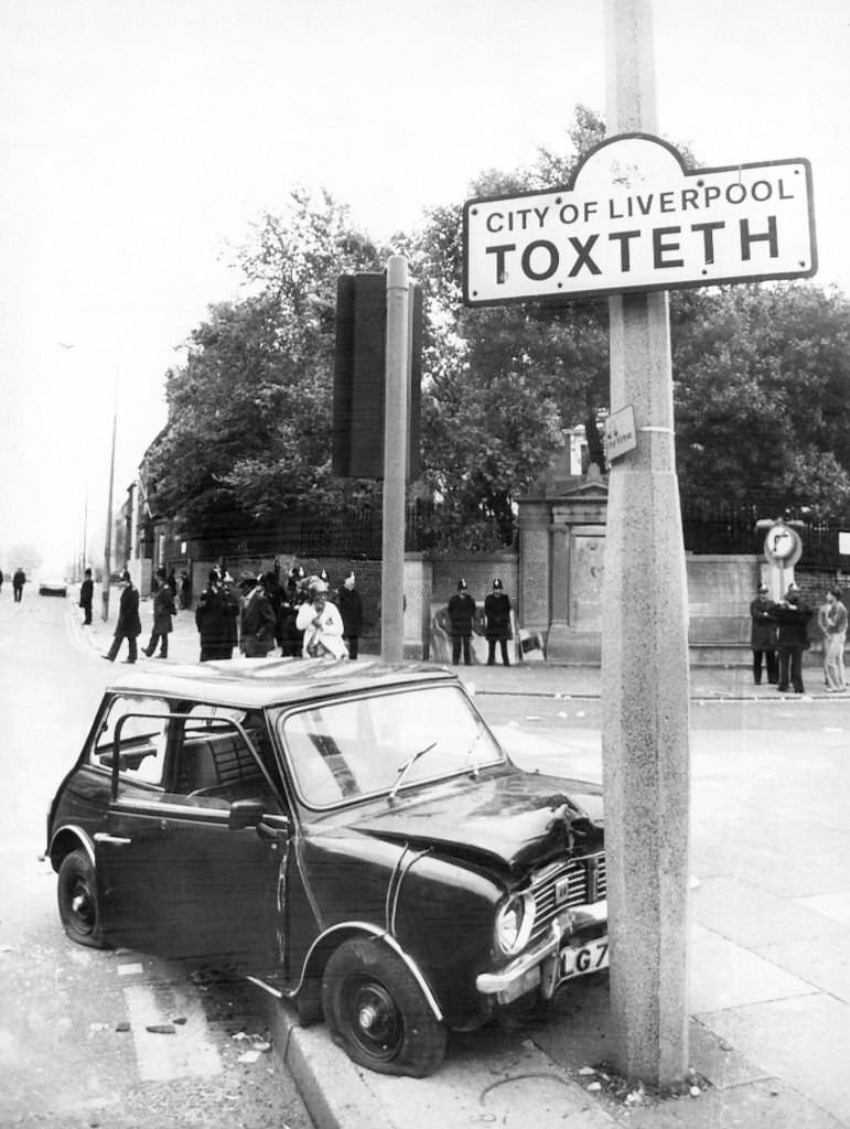#77 A wrecked car at the Toxteth boundary in Liverpool following riots, July 1981.