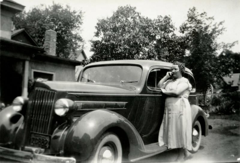 #12 A curly-haired lady in a white linen dress posing with a 1936 Packard 120 Sedan in front of the family home, 1938