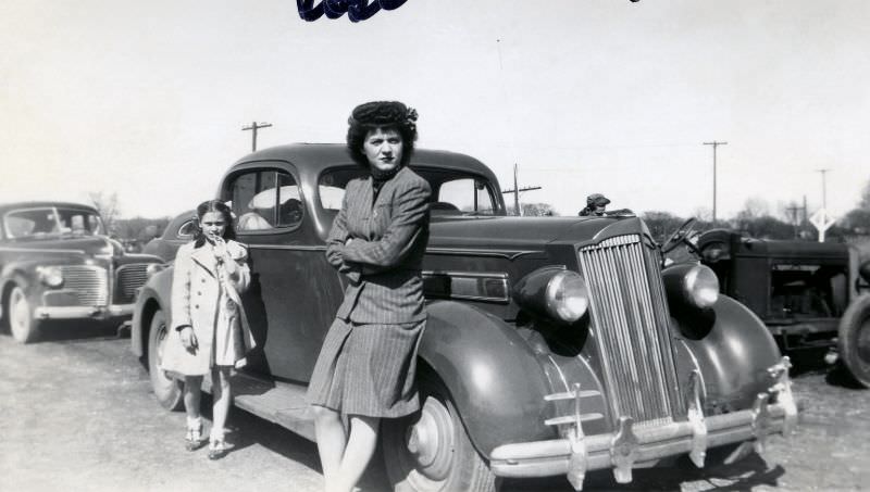 #21 A slightly grumpy-looking lady and her daughter posing with a 1936 Packard 120 Coupe on a dirt road in the countryside.