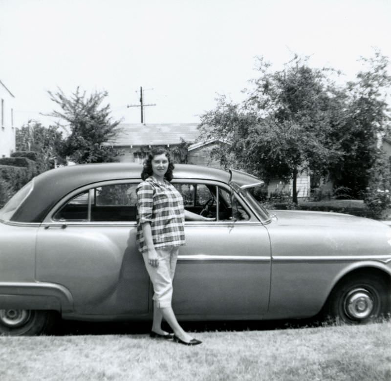 #22 A young expectant lady dressed in Capri pants and a checkered top posing with a 1951-52 Packard 200 Sedan in a suburban street, 1955