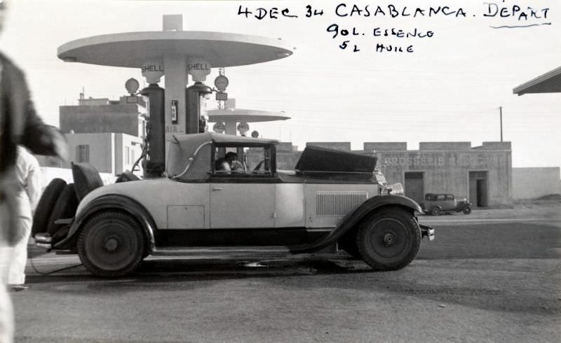 #8 A 1930 two-tone Packard Standard Eight Convertible Coupe convertible refueling at a Shell filling station in early morning sunlight, December 4, 1934