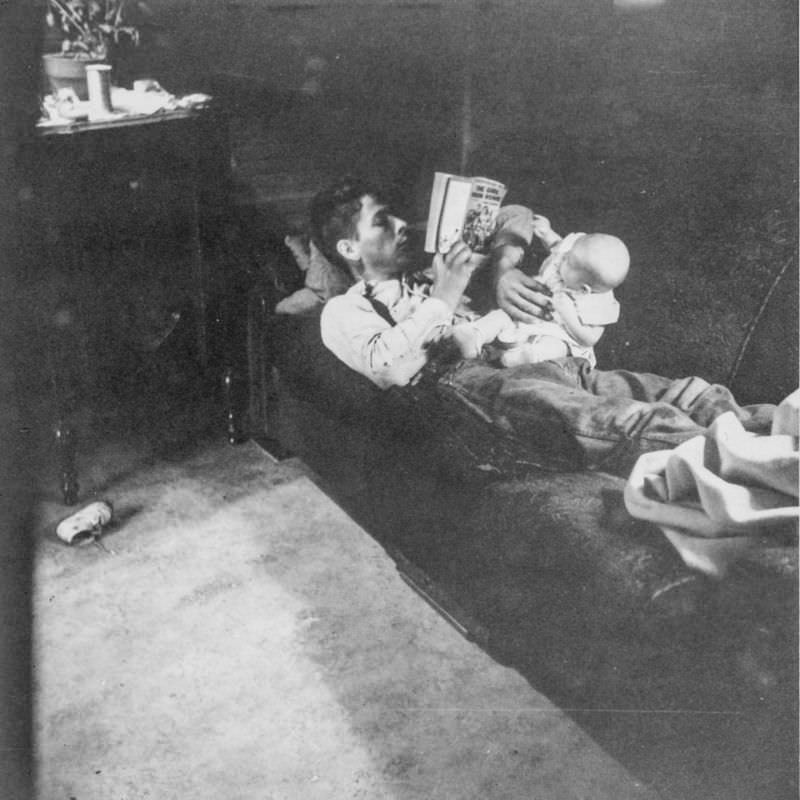 #21 Man holds baby while reading a book, July 1957