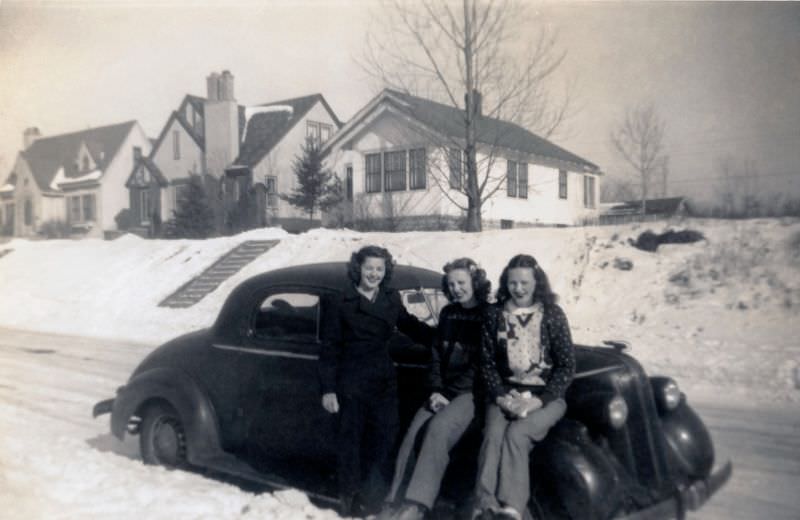Three ladies, probably a mother and her daughters, posing with a 1936 Pontiac Business Coupe on a snow-covered road on a sunny winter’s day, 1936
