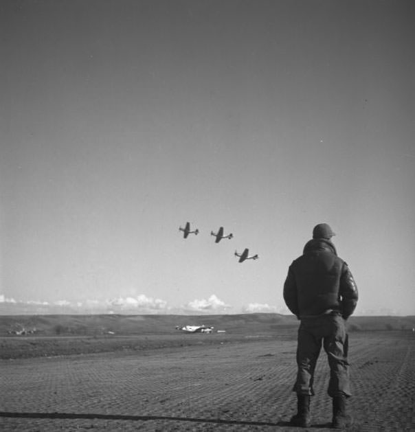 #4 A Tuskegee airman standing on an airfield, looking at airplanes